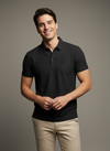Man wearing a black polo shirt and beige pants against a gray background